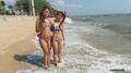 Girls standing in beach surf wearing bikinis